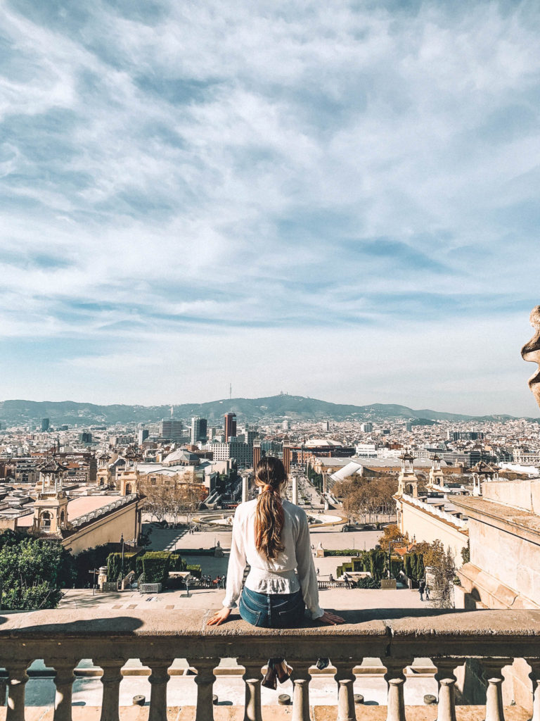 a girl sits on a wall and looks out on the view of place d'Espanya in Montjuic, Barcelona