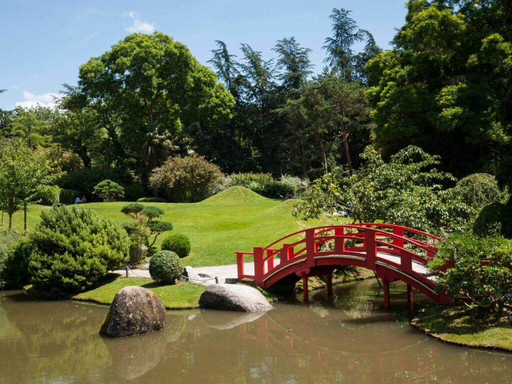 Red bridge and surrounding greenery at the Pierre Baudis Japanese Garden in Toulouse.