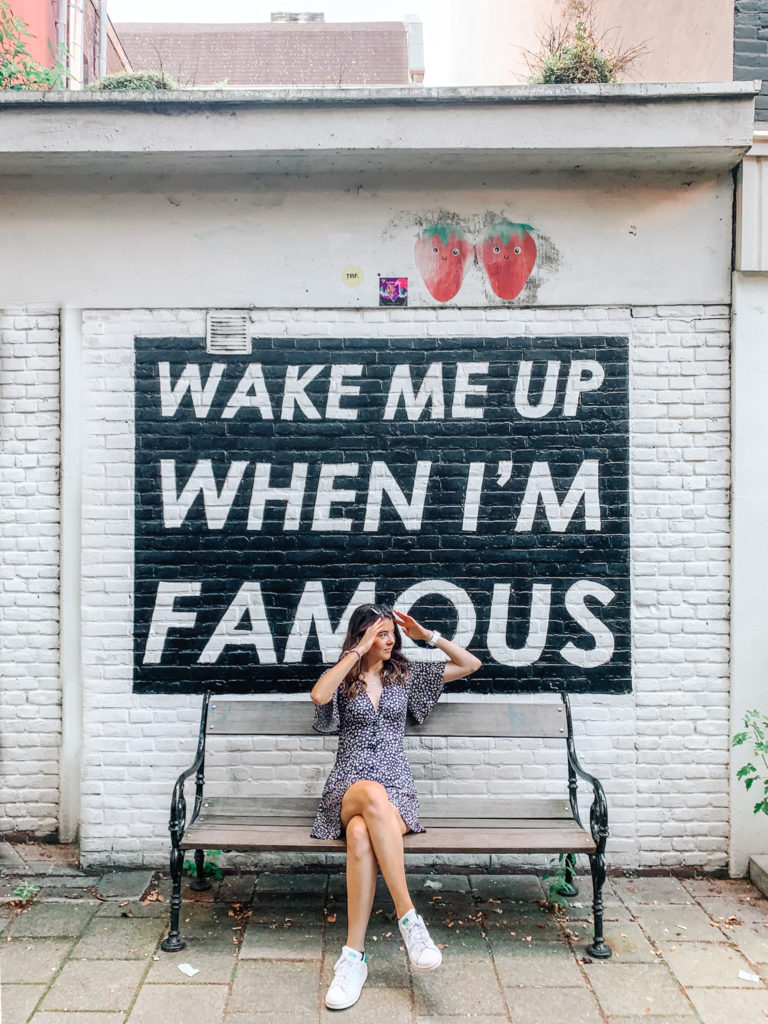 a girl poses in front of the Wake me up when i'm famous mural, one of the best photo spots in amsterdam