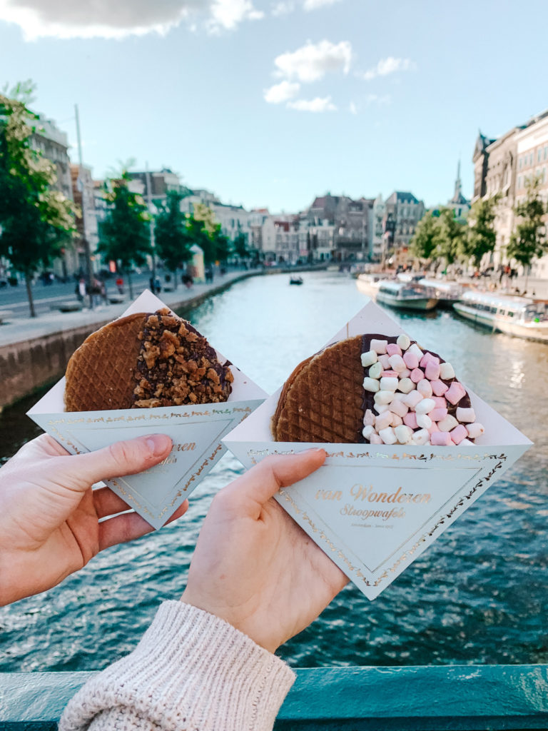 two hands hold stroopwafel from Van Wonderen Stroopwafels over a canal in Amsterdam