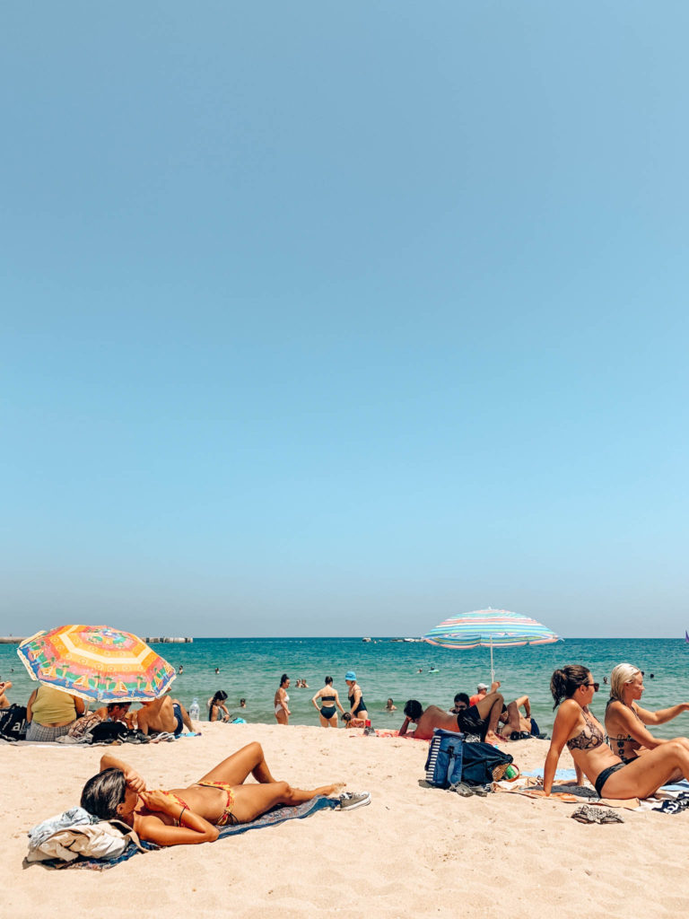 A sunny beach in Barcelona with parasols and many people sunbathing