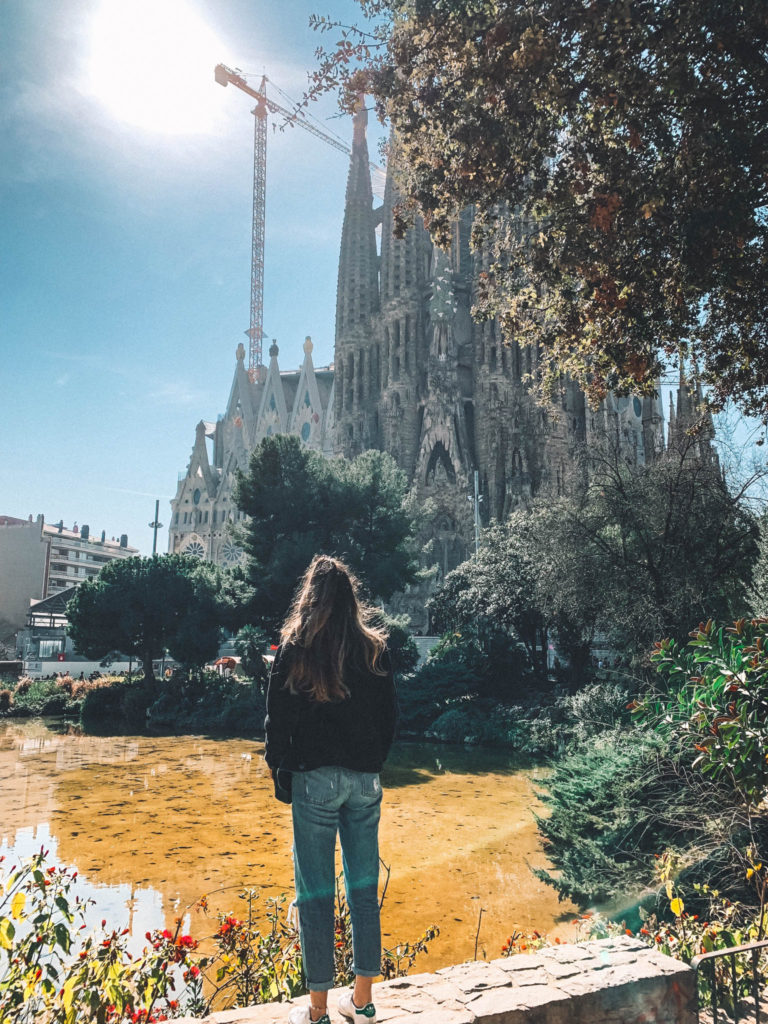 A girl looks at the Sagrada Familia in Barcelona from a viewpoint with a pond in front of her