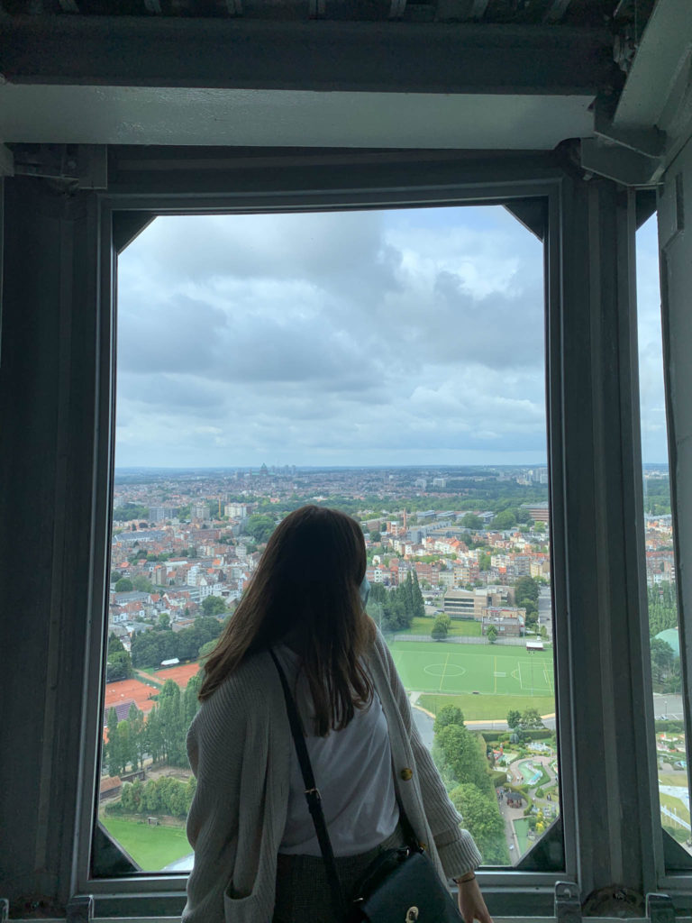 a girl sits in a window at the Atomium with a panoramic view of Brussels behind her