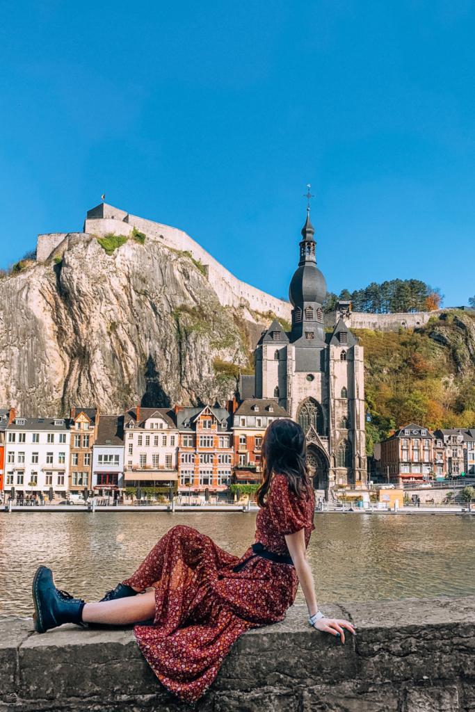 a girl in a red dress looks at the Dinant skyline across the meuse river