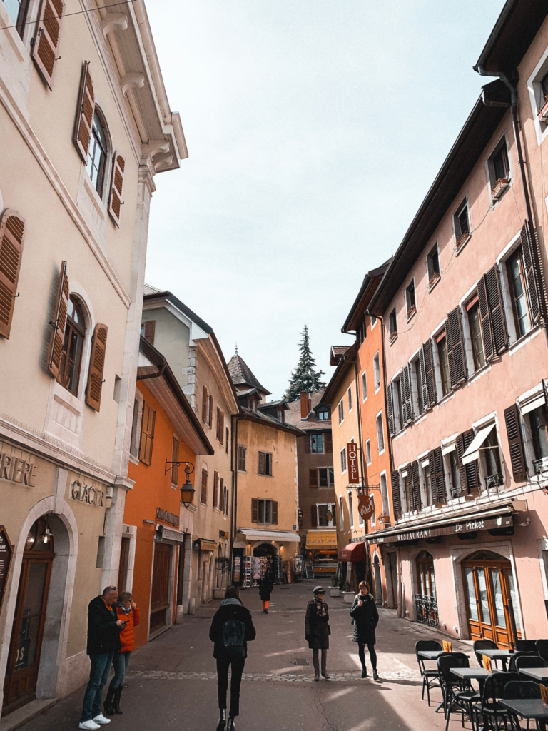 warm-toned houses on a street in Annecy's old town, with people walking around on the street