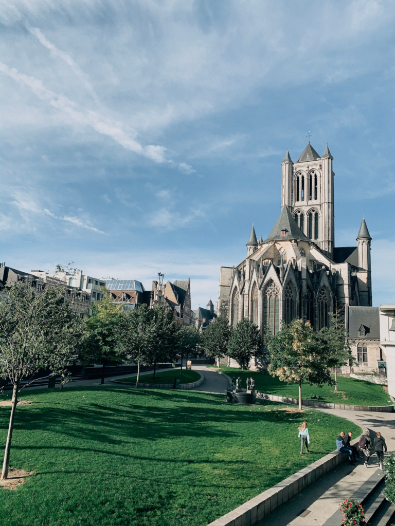 The rear of St Bavo's Cathedral in Ghent with a green park and people relaxing