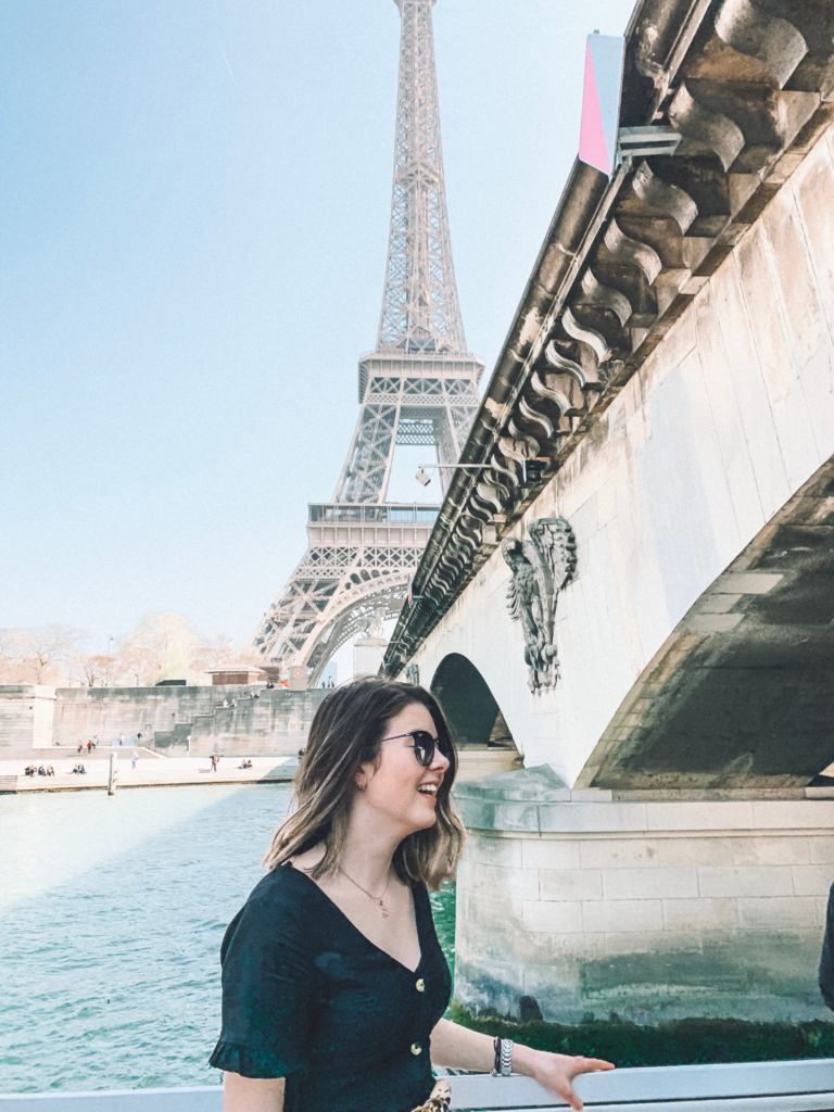 girl smiling on a boat passing under a bridge, with the Eiffel tower in the background