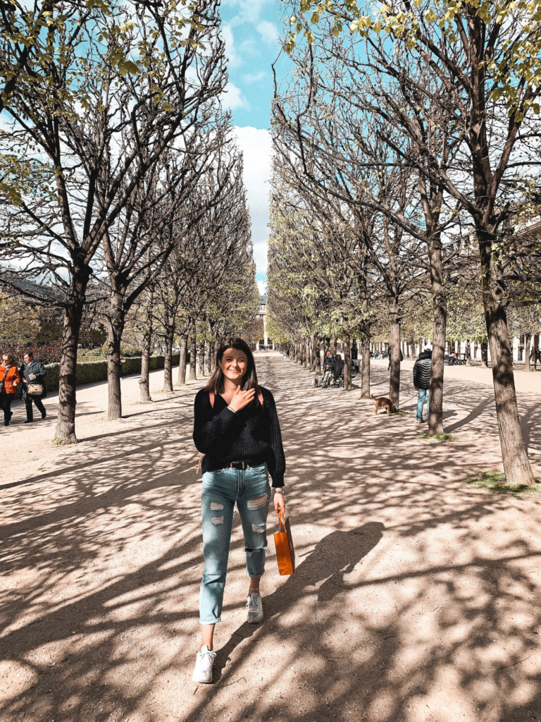 a girl smiles to the camera as she walks through Jardin du Palais Royal in Paris