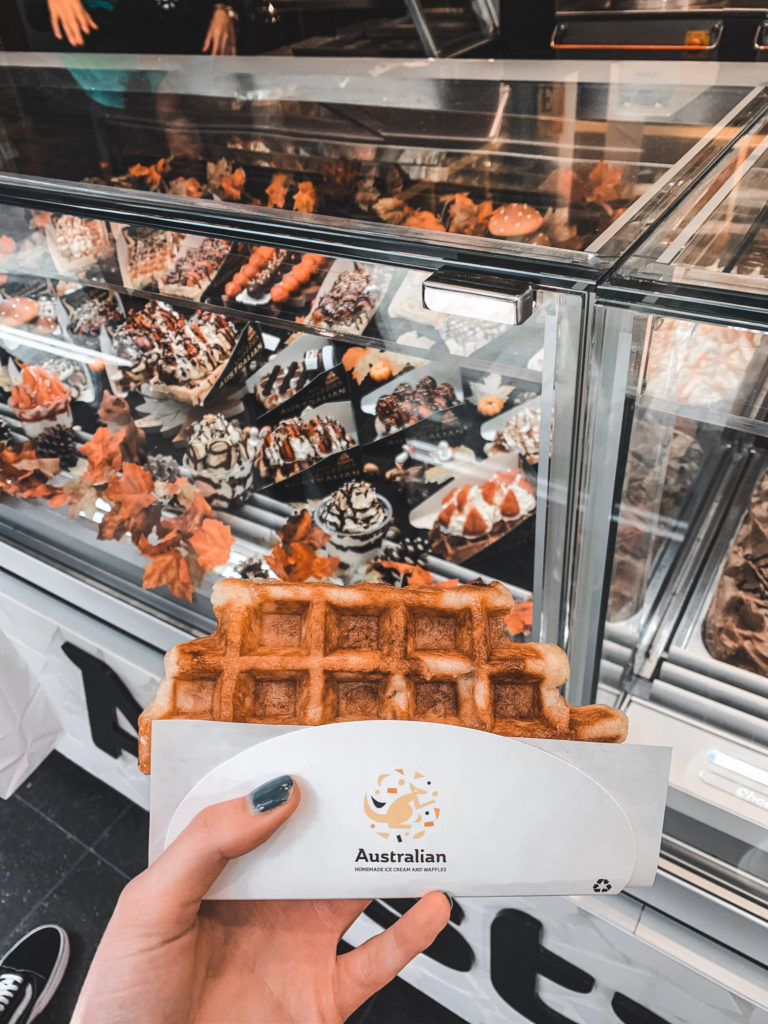 a Belgian waffle from Australian, Brussels, held in front of a counter with waffles on display