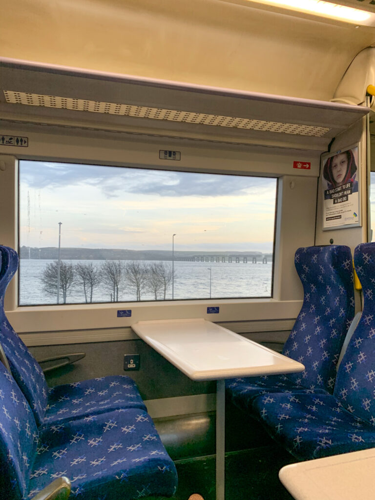 a train carriage with blue seats and a window view over water