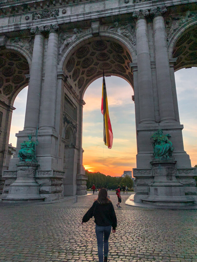 A girl walks towards the Cinquantenaire Arch and Cinquantenaire Park at sunset