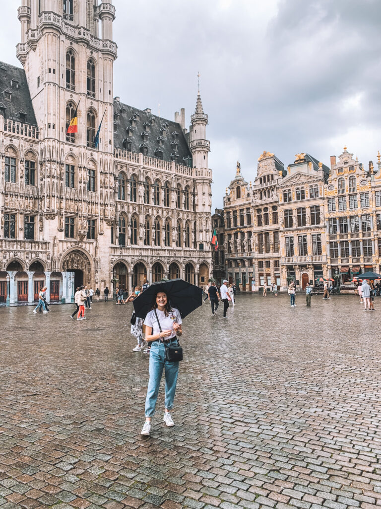 a girl holding an umbrella smiles in the middle of Grand Place, Brussels