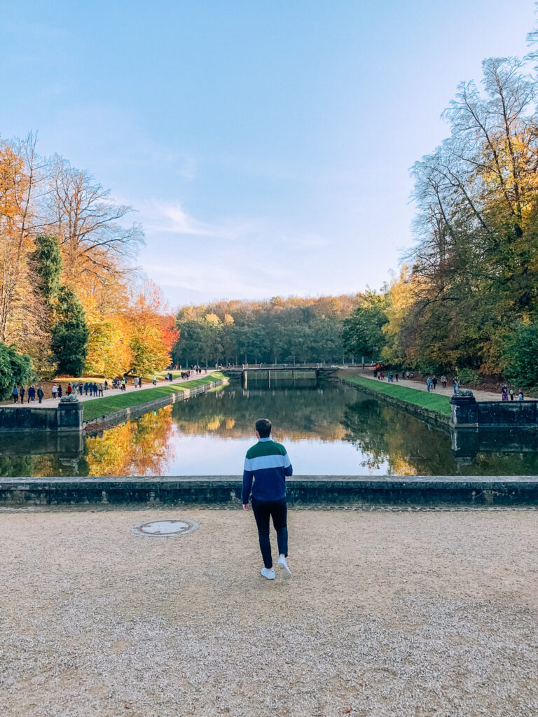 a man walks away from the camera in front of a large pond in Tervuren, Brussels