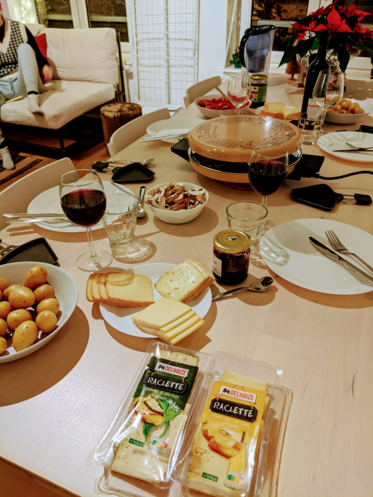 A dinner table set for raclette night - with raclette grills, cheese, wine, and various side dishes