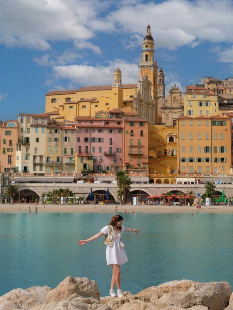 A girl standing on a rock looking out to the yellow houses of Menton, one of many towns on the French Riviera